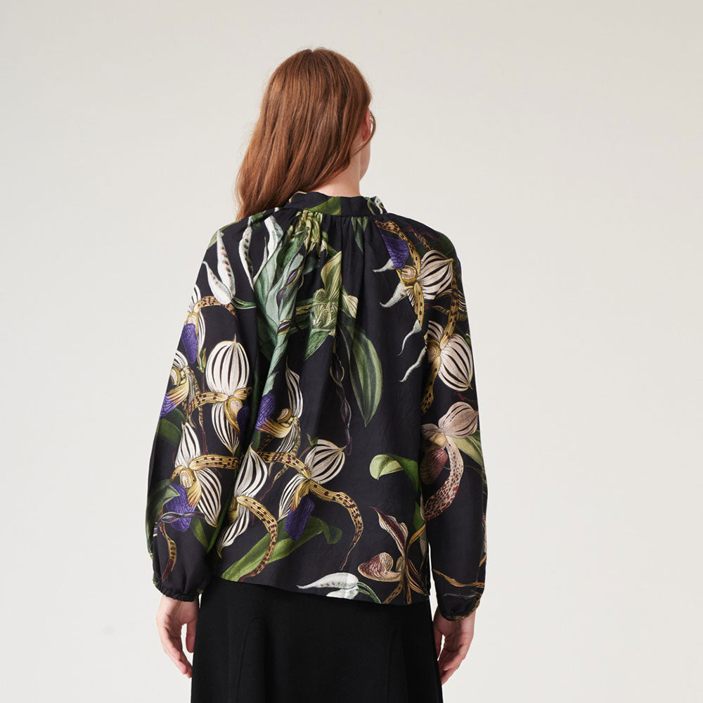 black pussy bow blouse shirt with orchid print in green, blue, ivory and yellow, worn with a black a line skirt
