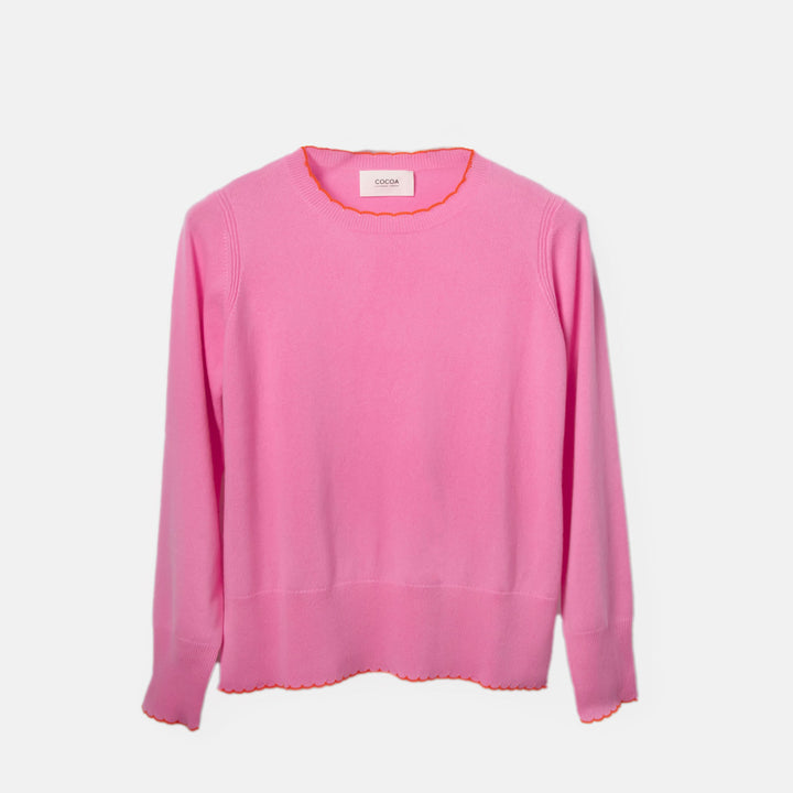pink sweater with orange scalloped trim at neck, cuff and hem on a light grey background