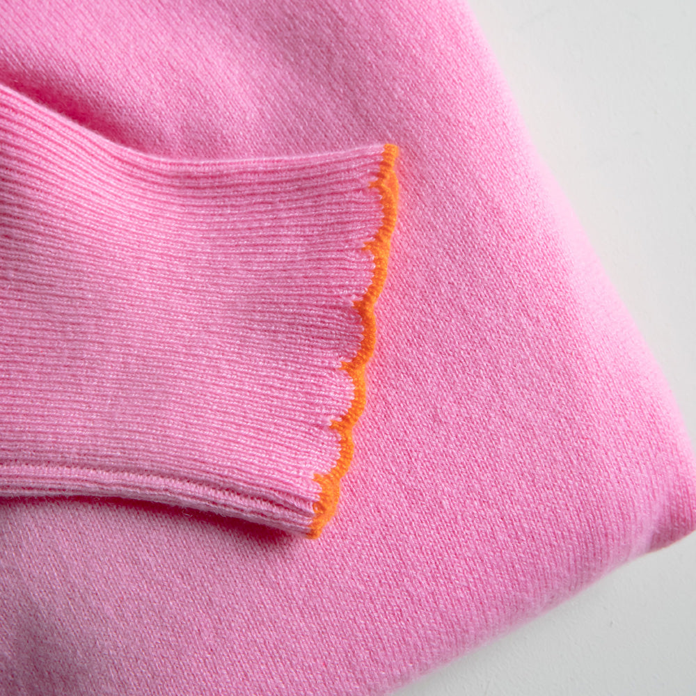 Close-up of pink jumper sleeve with orange trim on a light grey background