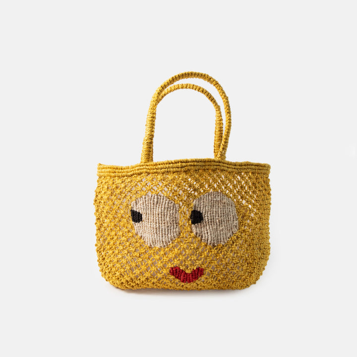 Yellow woven jute shopper bag with a face design on a white background