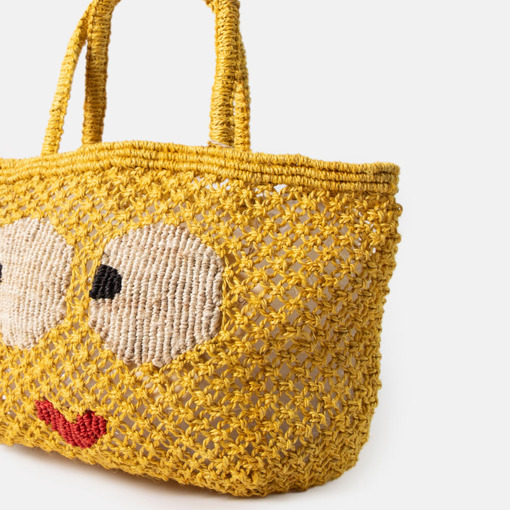 Yellow woven jute shopper bag with a face design on a white background