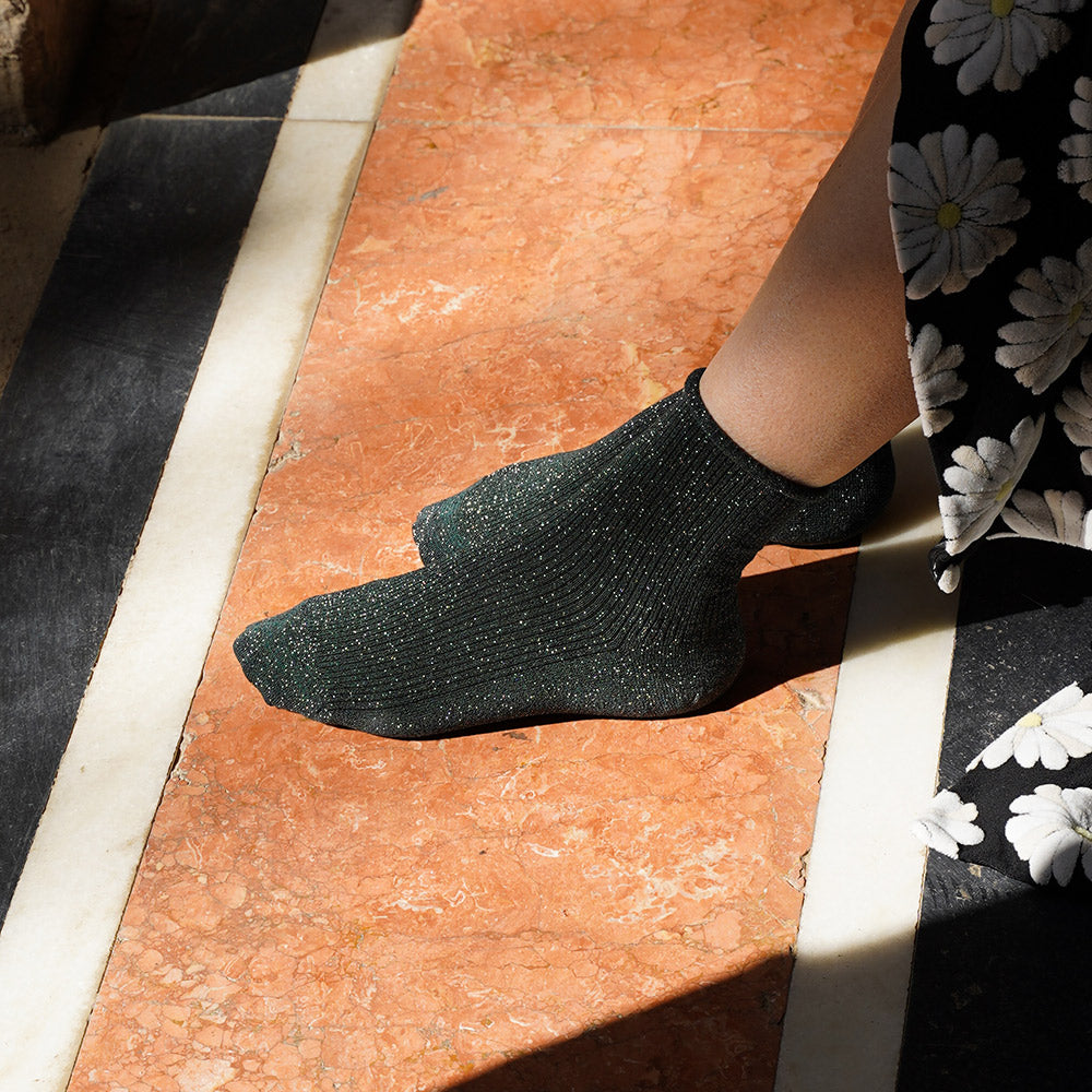 person wearing dark green ribbed sparkly socks with a floral skirt