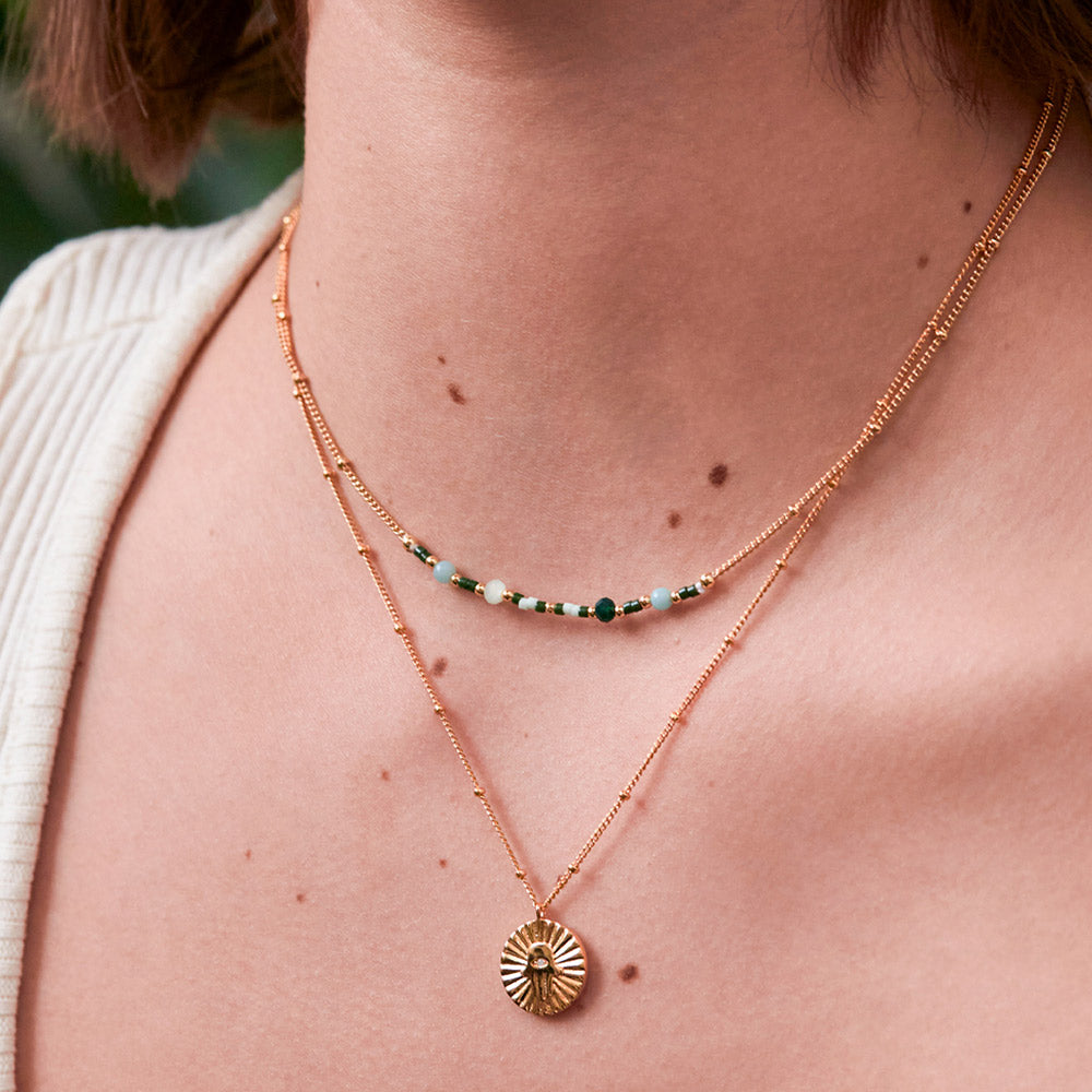 woman wearing a gold plated necklace with green enamel beads