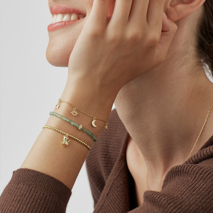 woman wearing a gold beaded bracelet with a waving lucky cat charm on a white background