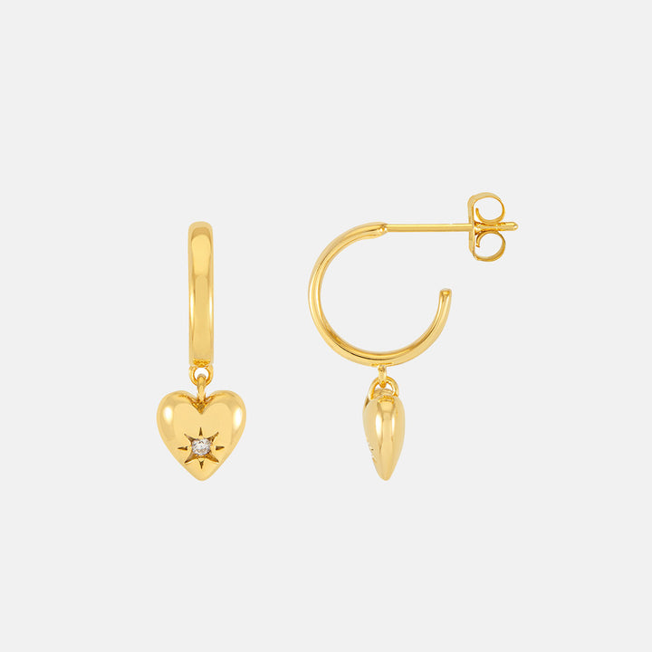 Gold hoop earrings with heart charms on a light grey background
