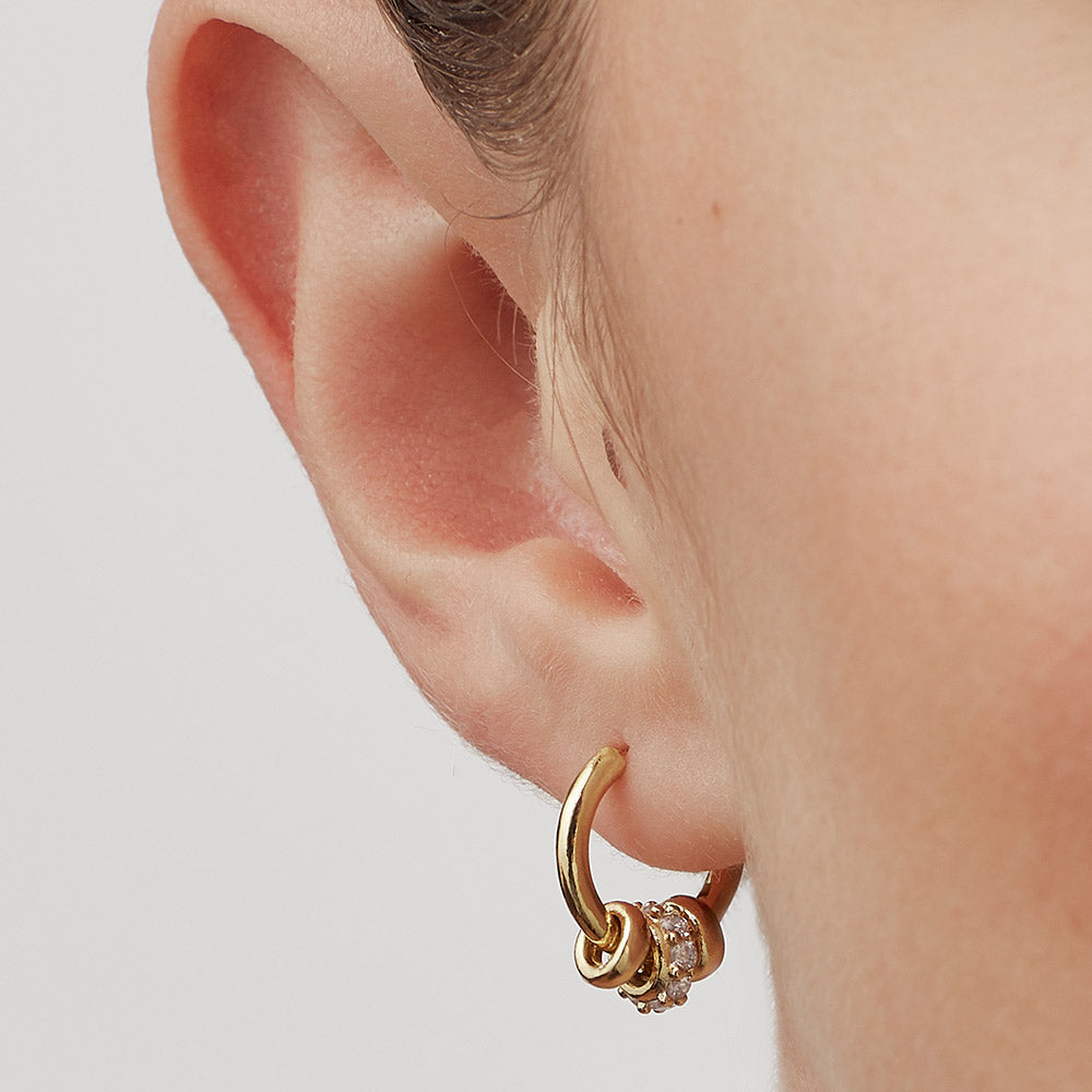 woman wearing gold huggie hoop earrings with 3 gold discs, one set with cubic zirconia