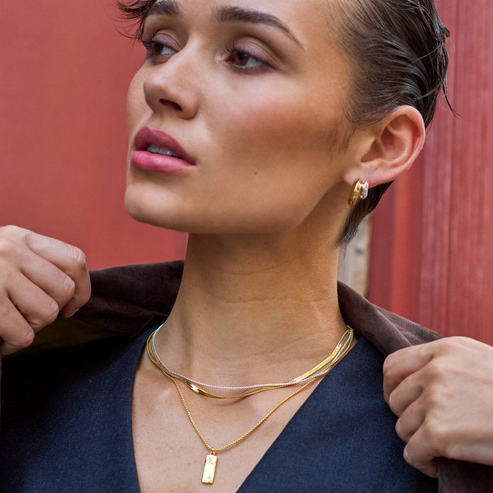 Woman wearing gold necklaces and earrings against a red background