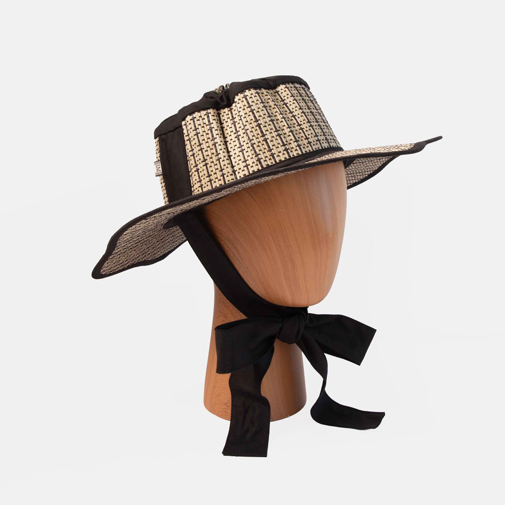 Black and beige straw hat on a mannequin head with a black ribbon against a white background