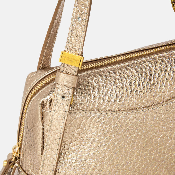 Gold handbag with matching strap on a light beige background