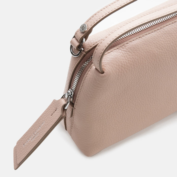 light pink leather handbag with a silver zip on a light grey background
