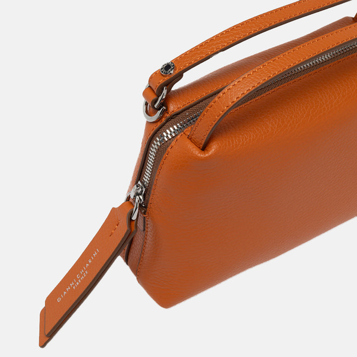 orange leather handbag with sliver zip on a light grey background