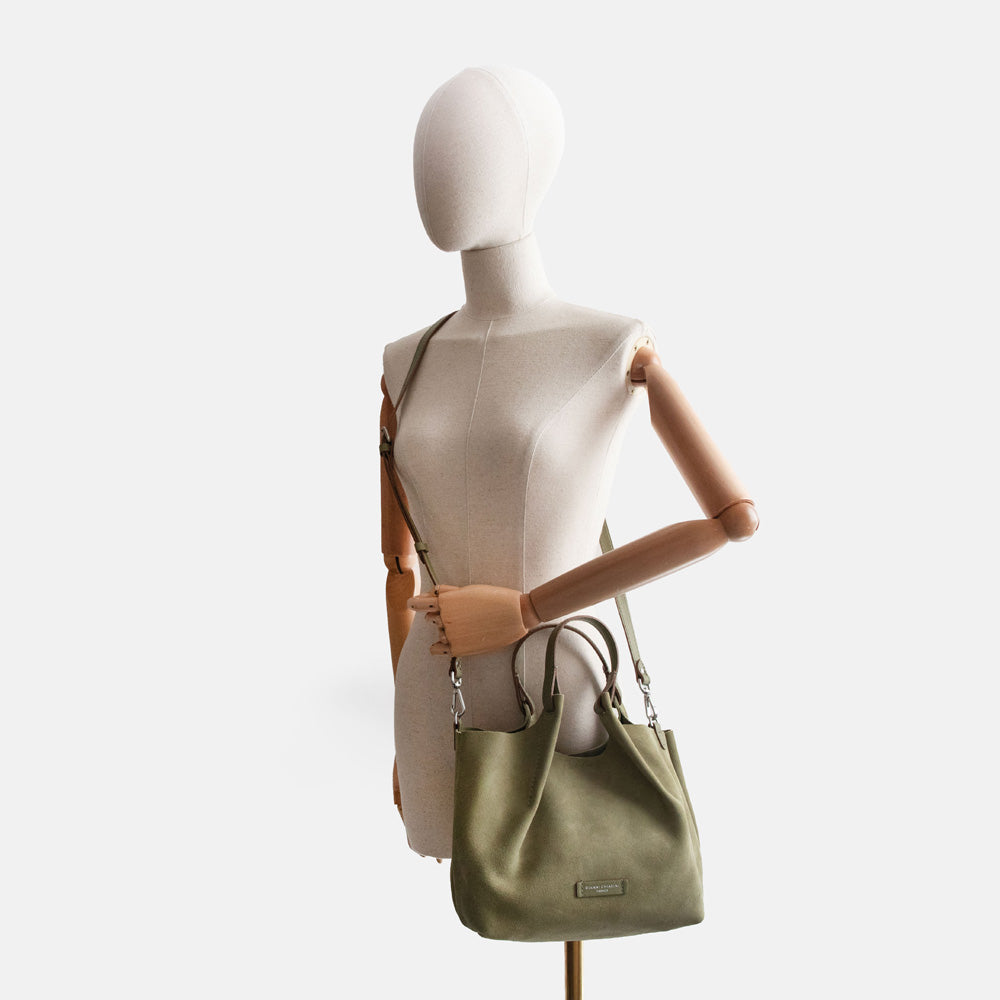 Mannequin wearing a green suede bucket style handbag with green leather handle and cross body strap