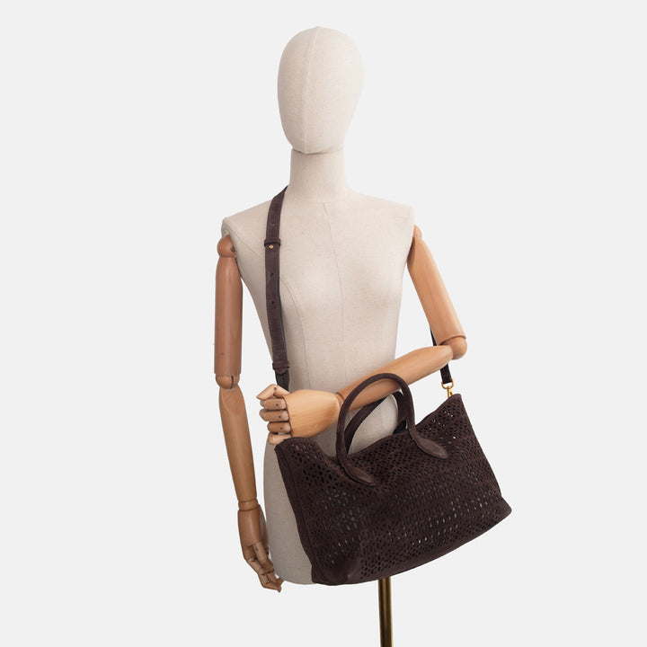 Mannequin holding a dark brown perforated suede handbag with brown leather grab handles on a white background