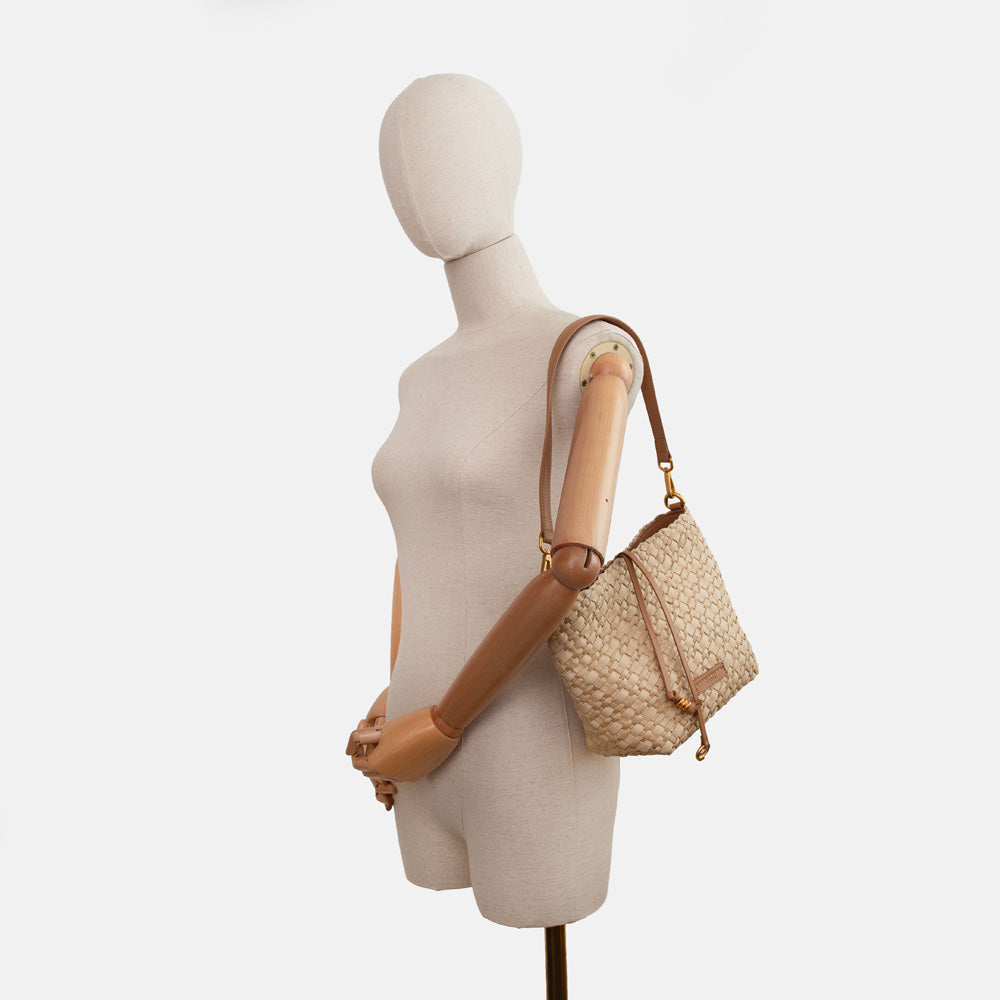 mannequin wearing a sand colour woven material handbag with light brown leather shoulder strap on a white background
