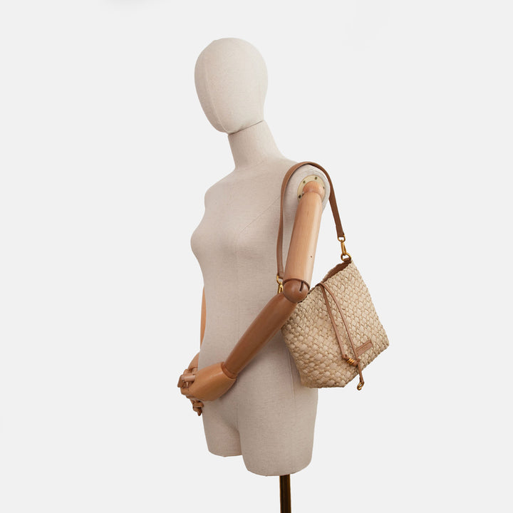 mannequin wearing a sand colour woven material handbag with light brown leather shoulder strap on a white background