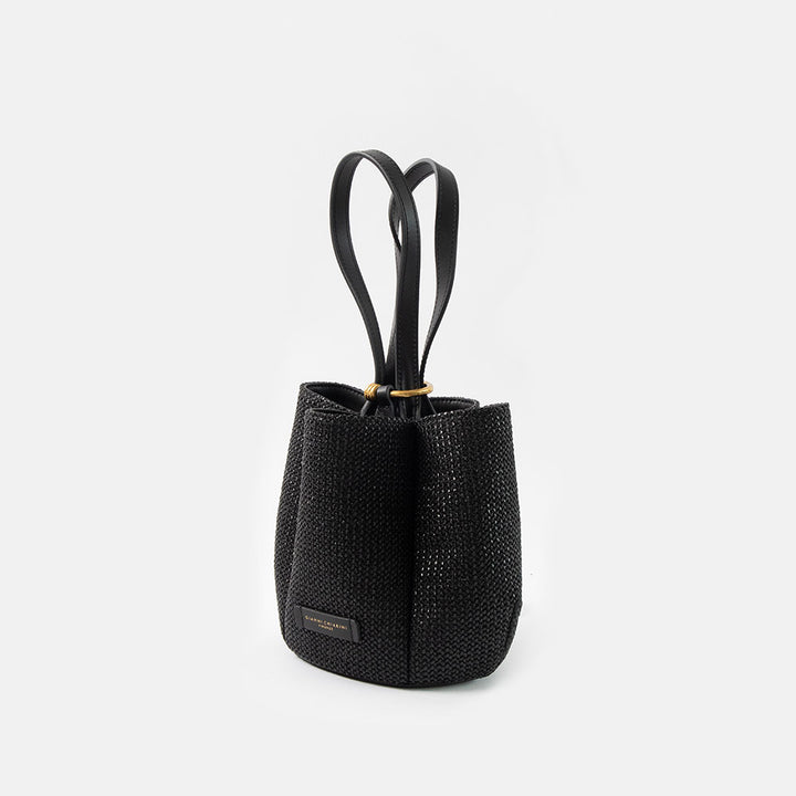 black woven straw bucket handbag with black leather shoulder straps and gold ring closure on a white background