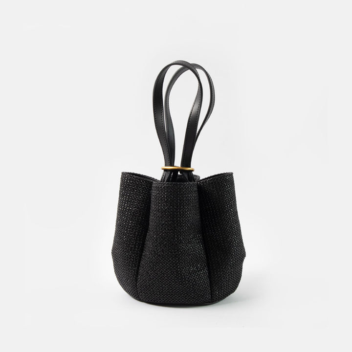 black woven straw bucket handbag with black leather shoulder straps and gold ring closure on a white background
