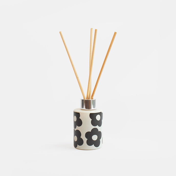 A ceramic reed diffuser bottle with a black and white floral pattern, filled with natural wood reeds, set against a clean white background.