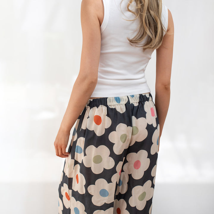 Person wearing a white tank top and floral pants on a plain background