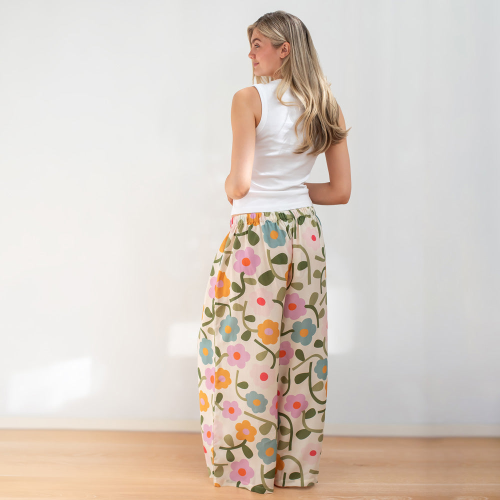 Woman wearing a white sleeveless top and floral pants against a plain background