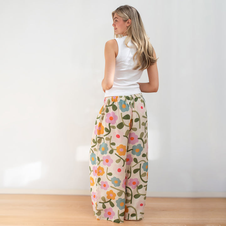 Woman wearing a white sleeveless top and floral pants against a plain background