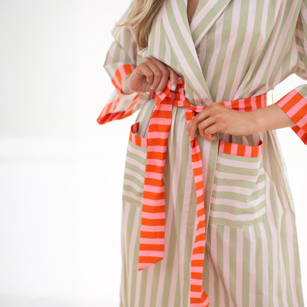 Person wearing a green and white striped robe with an orange and white striped sash on a white background