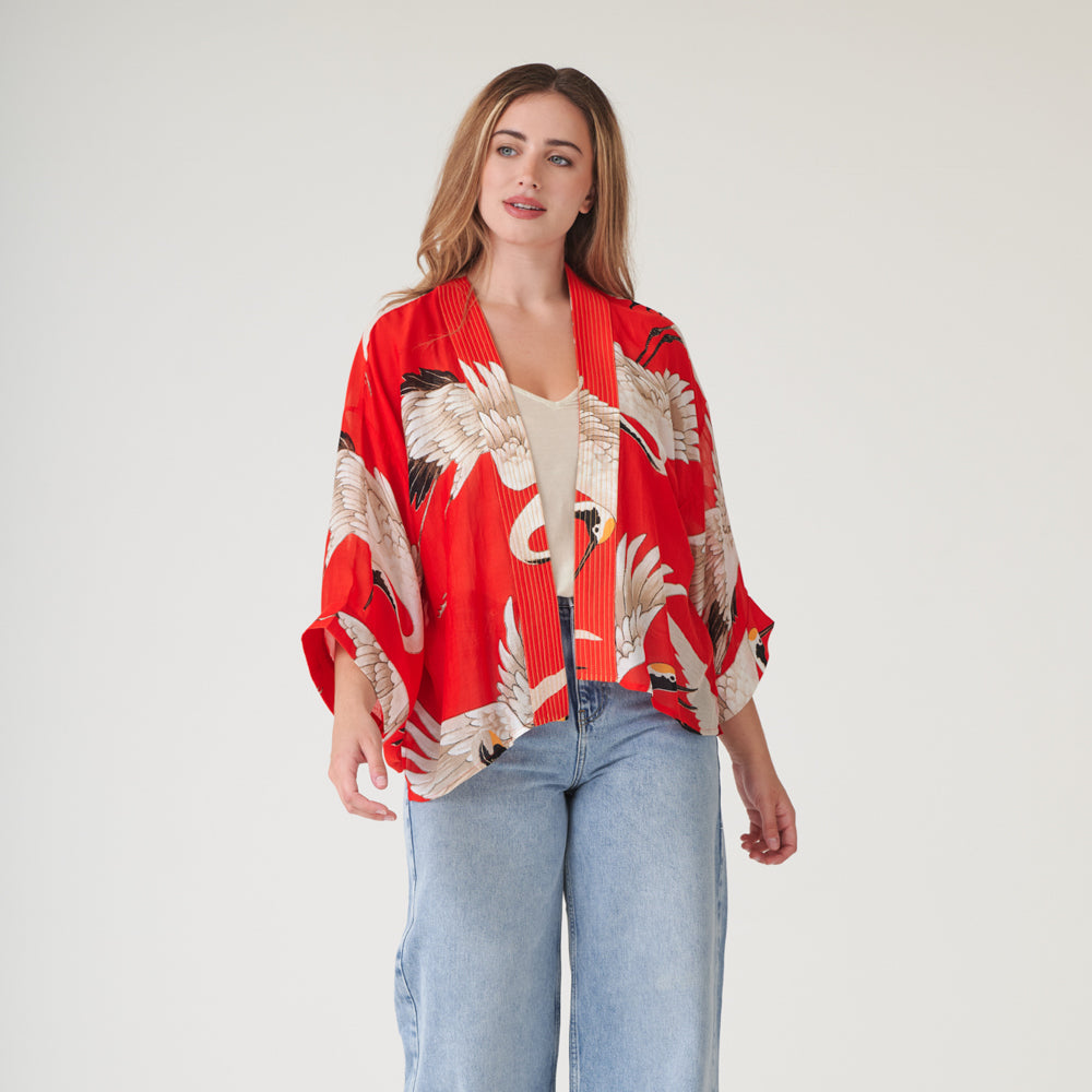woman wearing a short kimono with white storks on a bright red base over a white t-shirt with light wash jeans