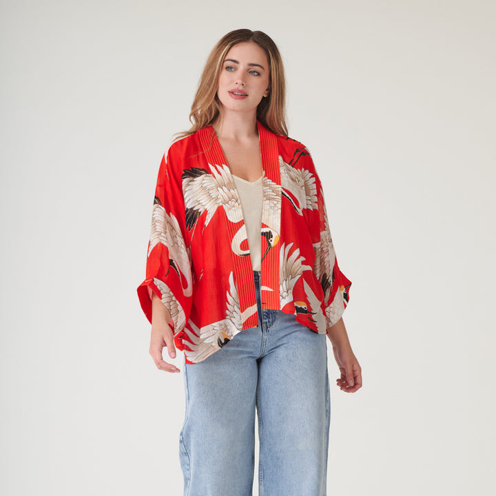 woman wearing a short kimono with white storks on a bright red base over a white t-shirt with light wash jeans
