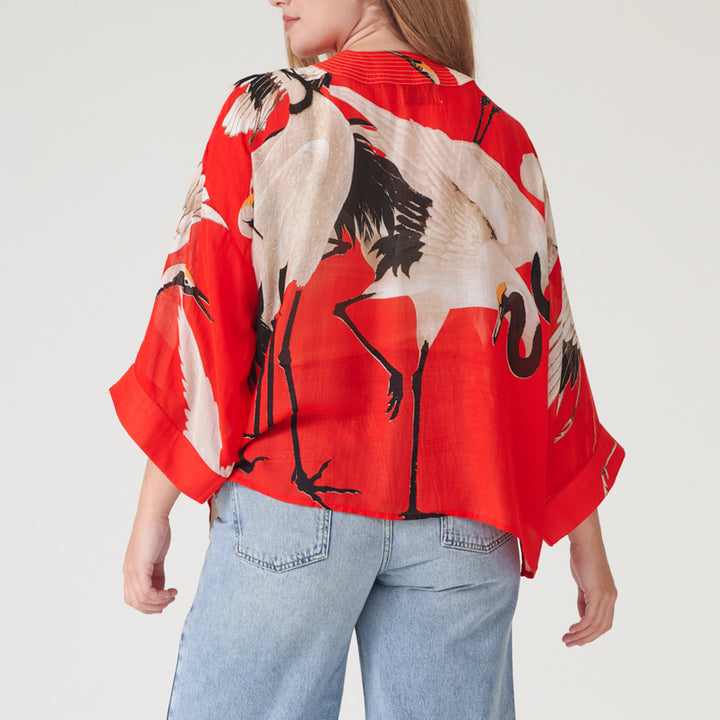 woman wearing a short kimono with white storks on a bright red base with light wash jeans