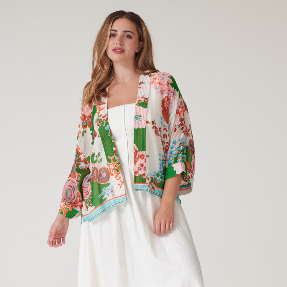 woman wearing a short kimono on orange and pink floral design on a green and stone base over a white dress