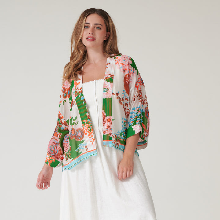 woman wearing a short kimono on orange and pink floral design on a green and stone base over a white dress