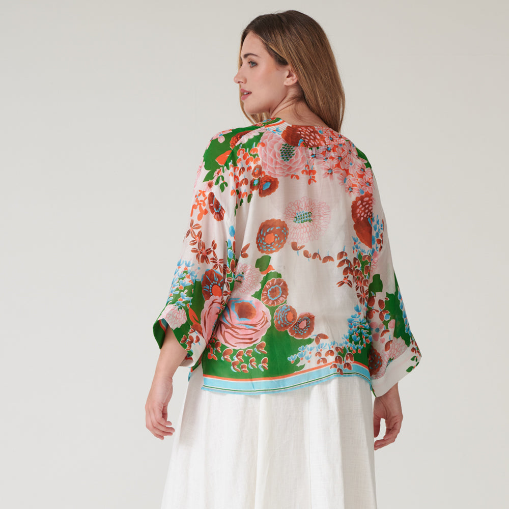 woman wearing a short kimono on orange and pink floral design on a green and stone base over a white dress