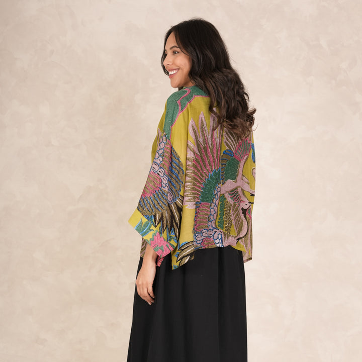 woman wearing a short kimono with pink, green & blue cranes design on an olive base with a black skirt