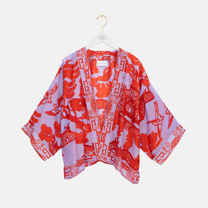 women's short kimono in japanese style design in bright red on lilac, on a coat hanger against a white background