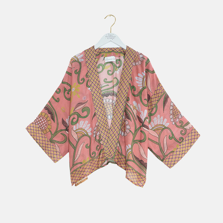 short kimono in dusky pink with floral design on a coat hanger against a white background