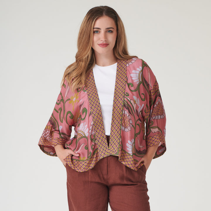 woman wearing a pink floral design short kimono with brick red trousers against a white background