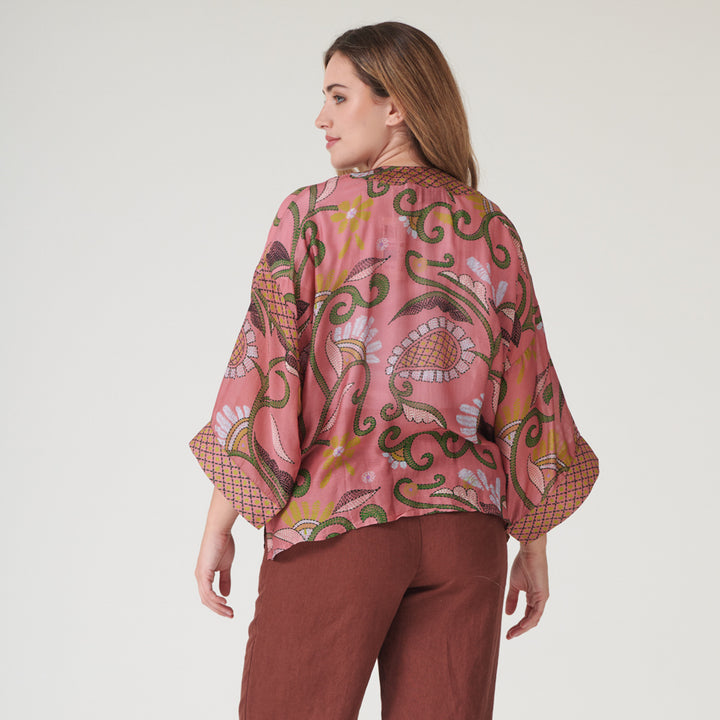 woman wearing a pink floral design short kimono with brick red trousers against a white background
