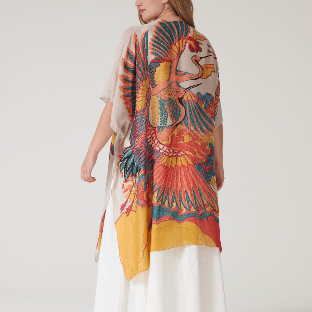 Woman wearing a colourful throwover garment with a large bird design on a plain background