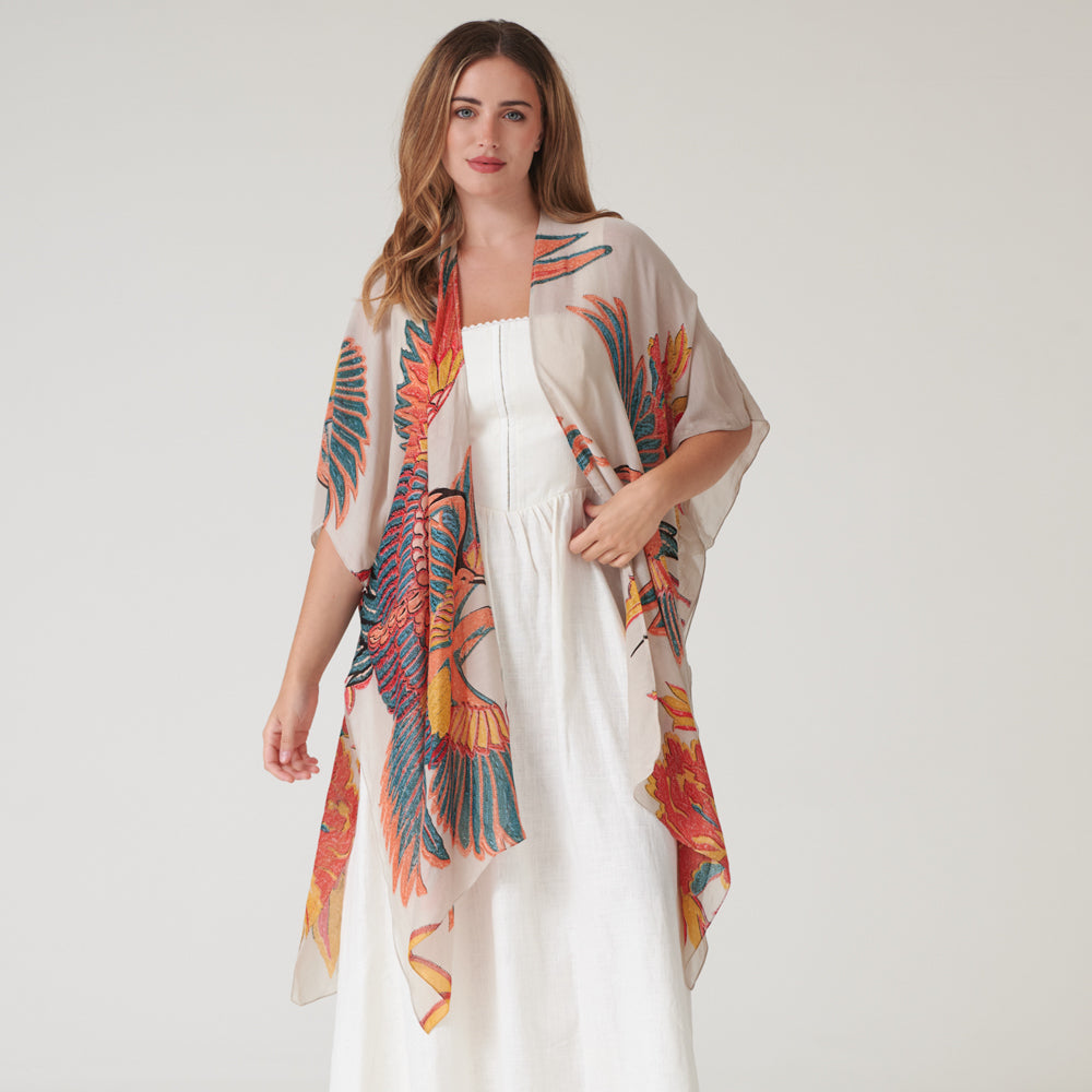 Woman wearing a colourful throwover garment with a large bird design on a plain background
