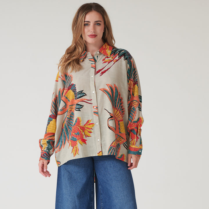 woman wearing an oversized long-line shirt in colourful crane print on a stone base with blue jeans