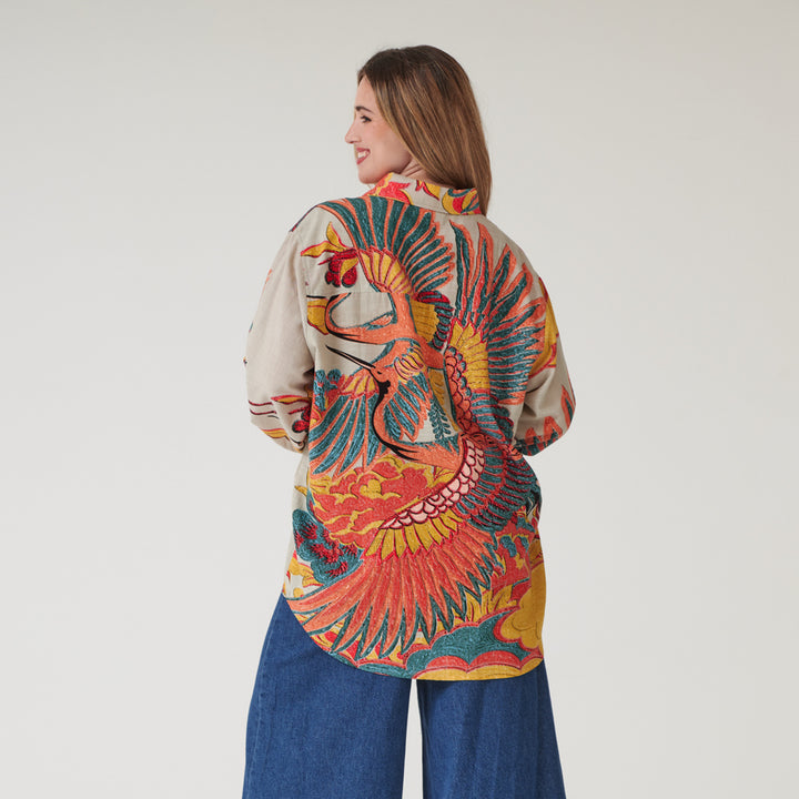 woman wearing an oversized long-line shirt in colourful crane print on a stone base with blue jeans
