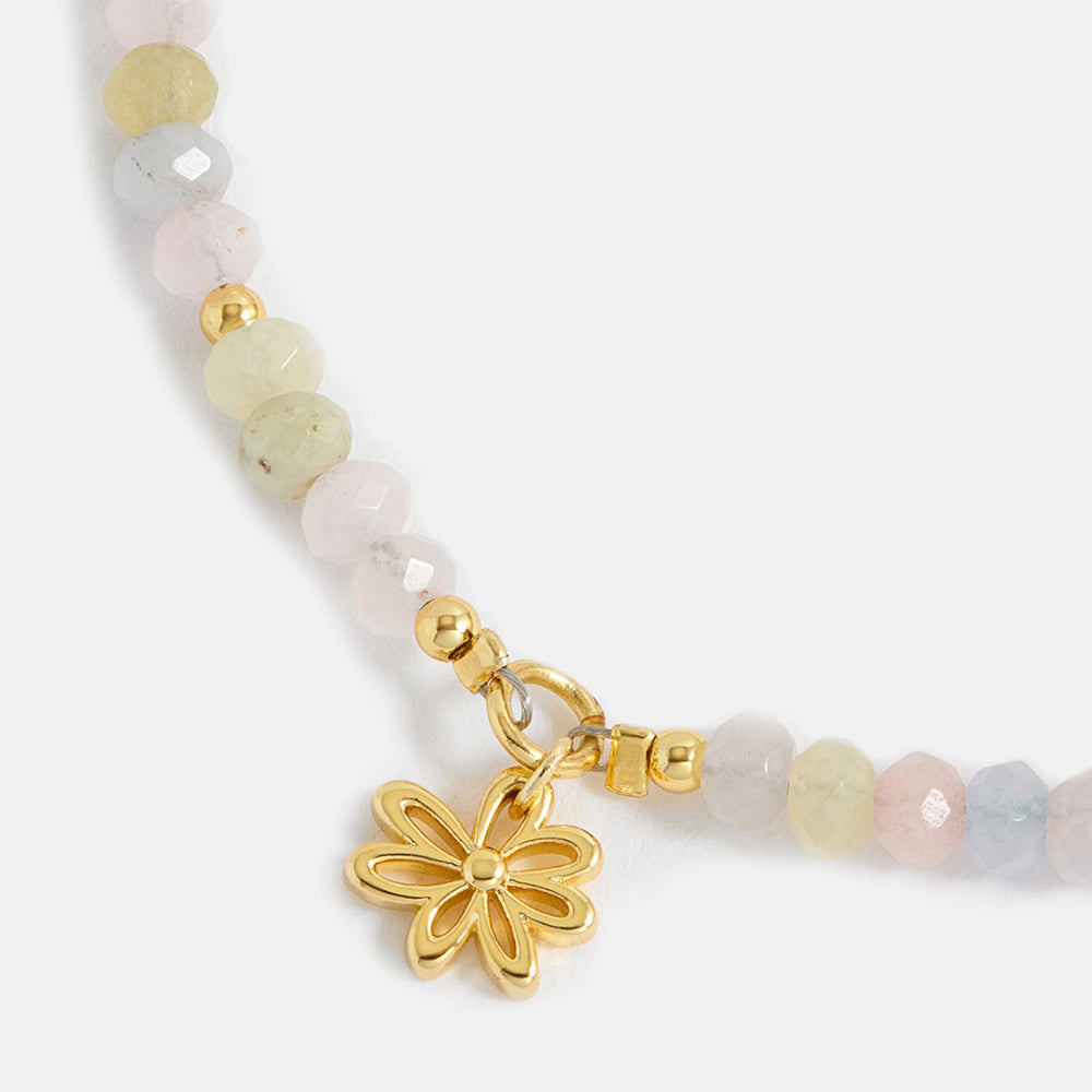 Beaded bracelet with a gold flower charm on a white background
