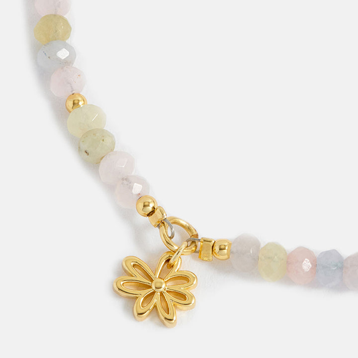 Beaded bracelet with a gold flower charm on a white background