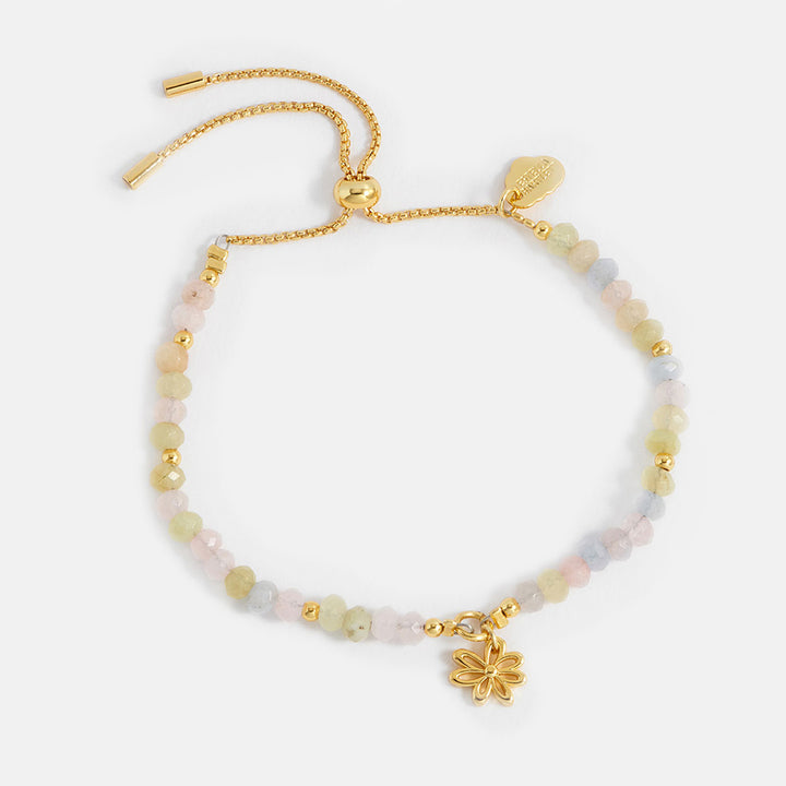 Gold bracelet with beaded chain and flower charm on a white background