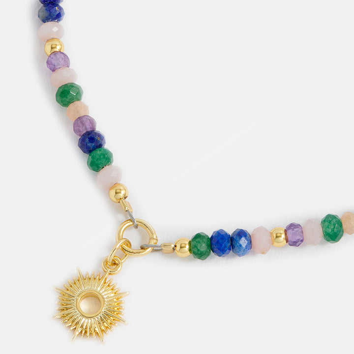 Multicolored beaded bracelet with a gold sun charm on a white background