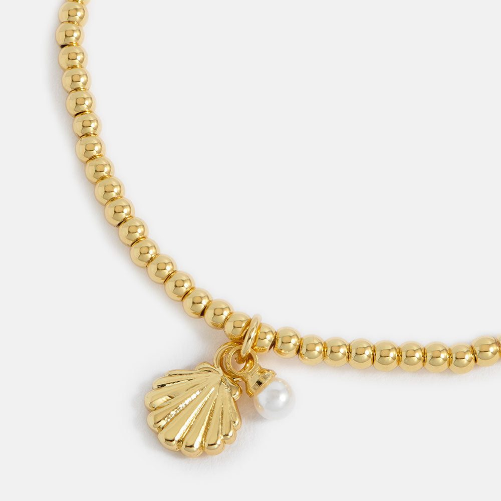Gold beaded bracelet with a shell charm and pearl on a white background