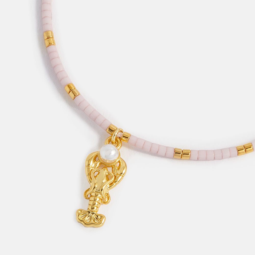 close up of a bracelet with pink beads and gold lobster charm on a white background