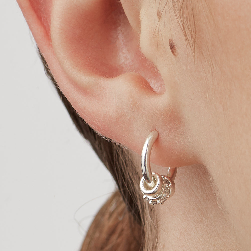 Silver hoop earring worn on an ear with a neutral background