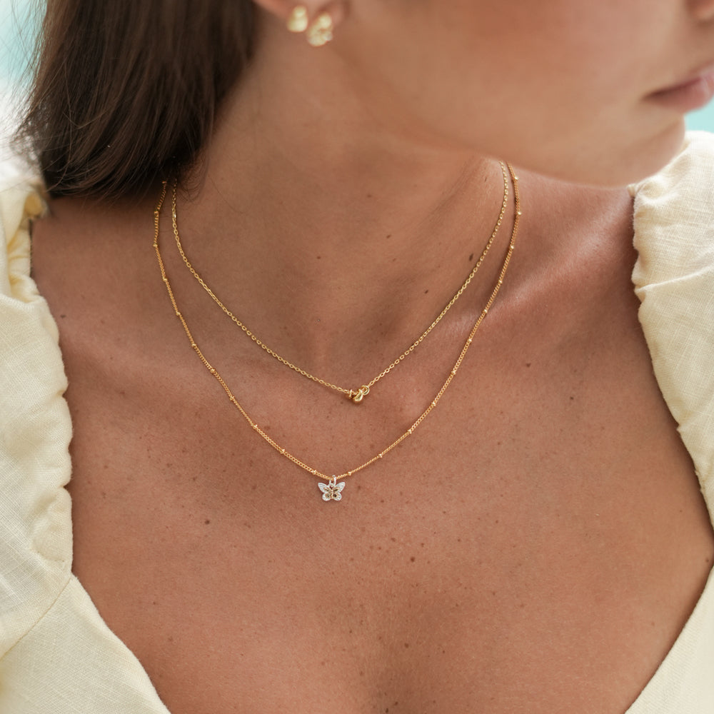 woman wearing 2 gold necklaces with teardrop and flower charms