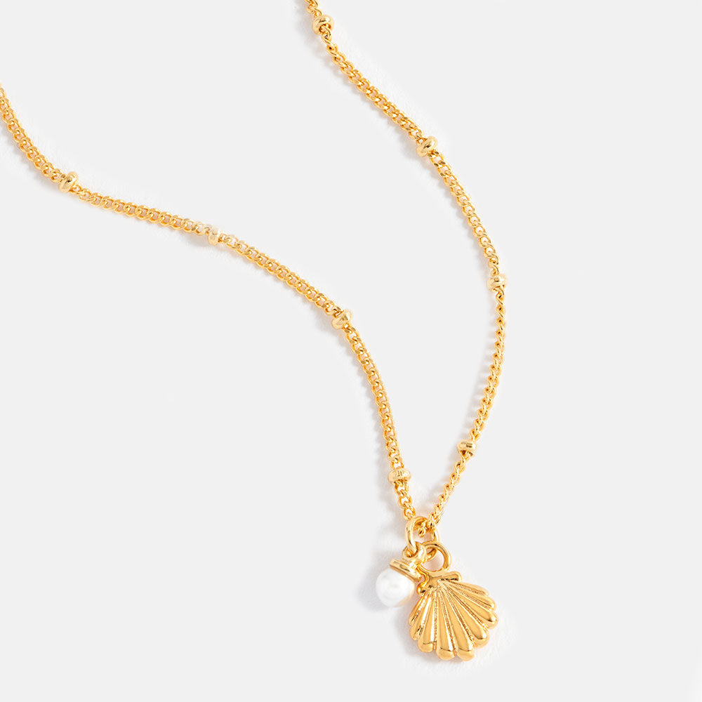 Gold necklace with shell and pearl charm on a white background
